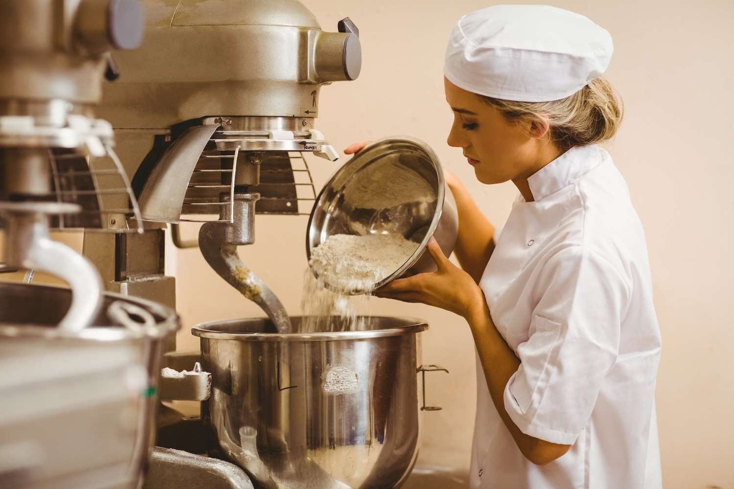a woman in a chef's uniform pouring flour into a mixer