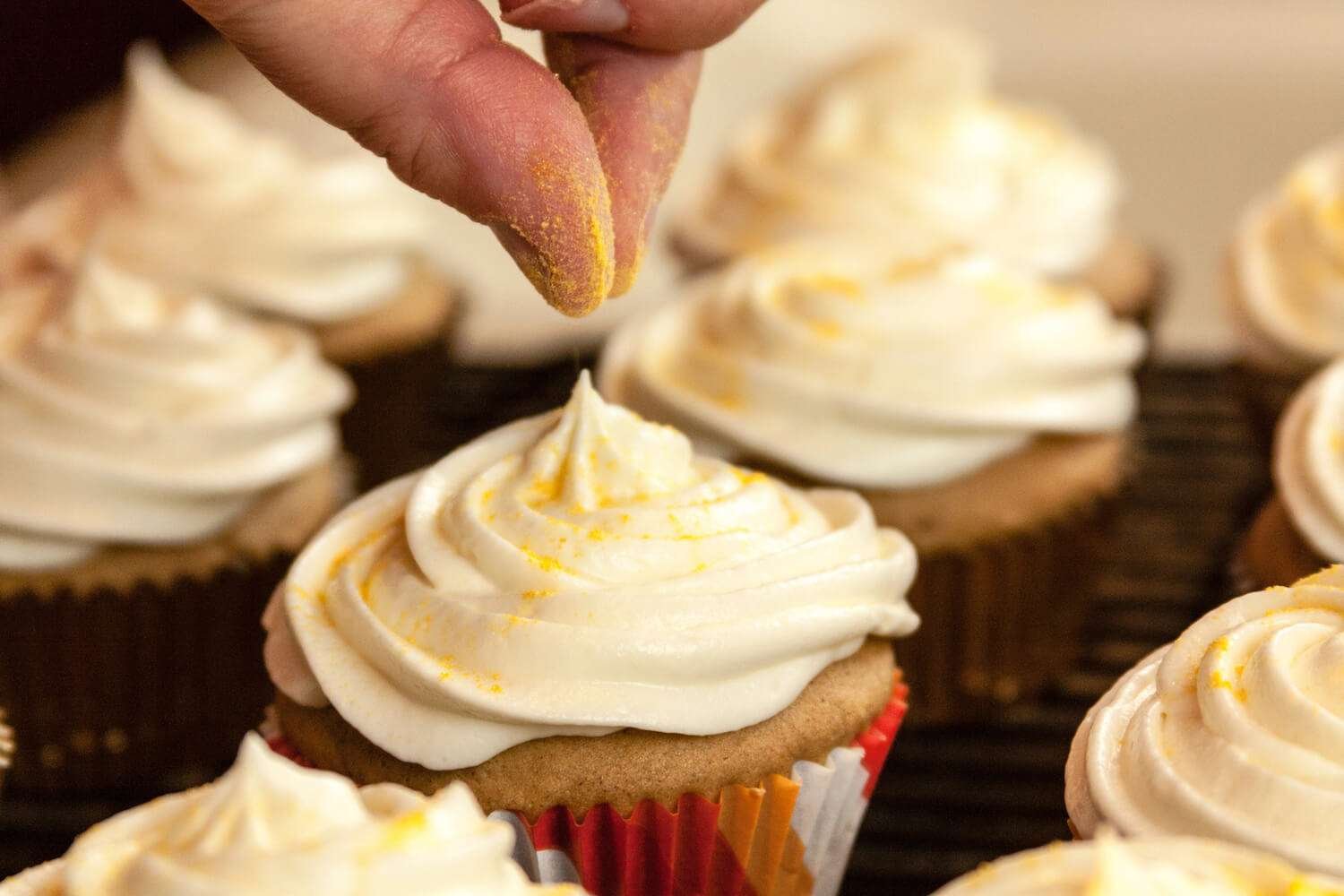 a person sprinkling yellow powder on a cupcake