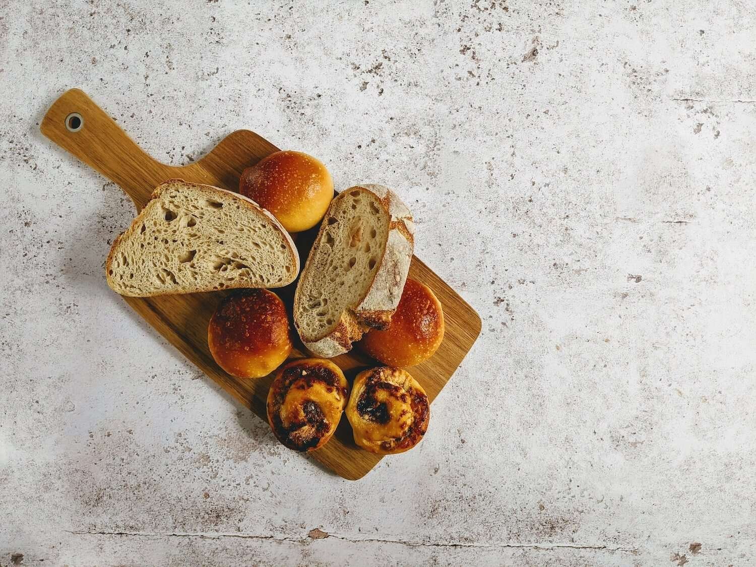 a wooden cutting board with sourbread and rolls