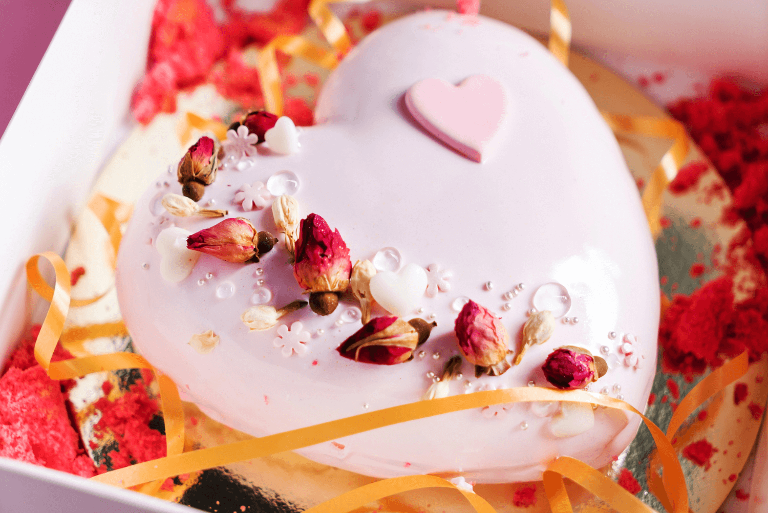a heart shaped cake with flowers and ribbons