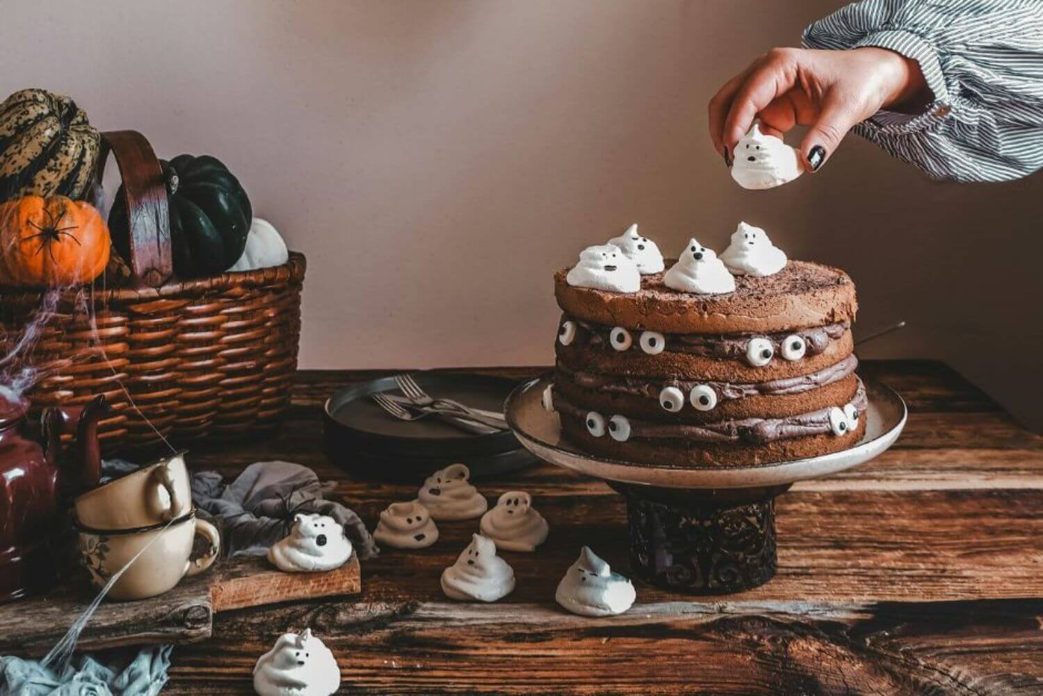 a person putting ghost meringues on a Halloween cake